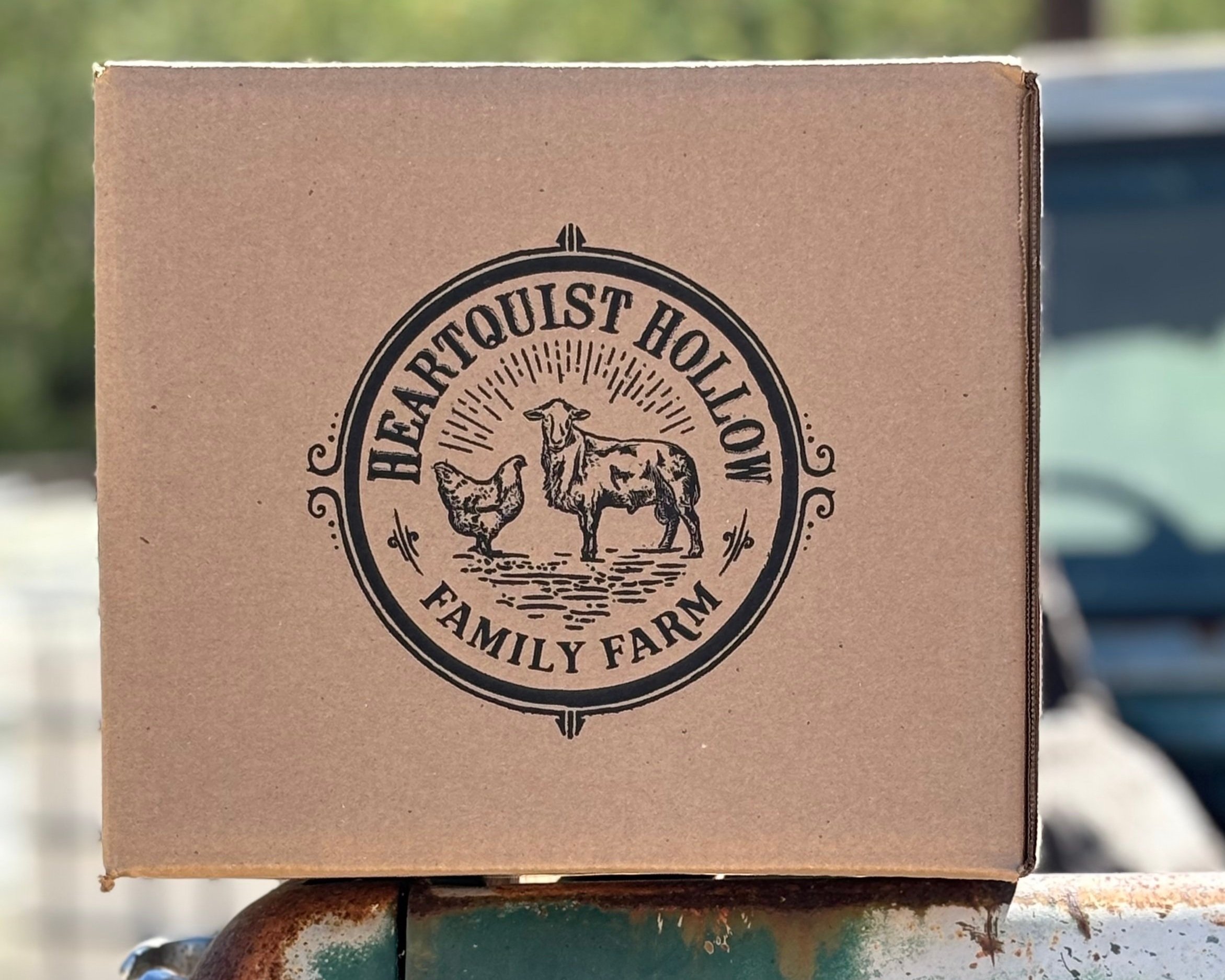 Cardboard box featuring the Heartquist Hollow Family Farm logo, depicting a chicken and cow, symbolizing farm-fresh produce and family-owned agriculture.